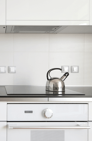 a stainless teakettle rests on a glass stovetop in a pristine contemporary kitchen