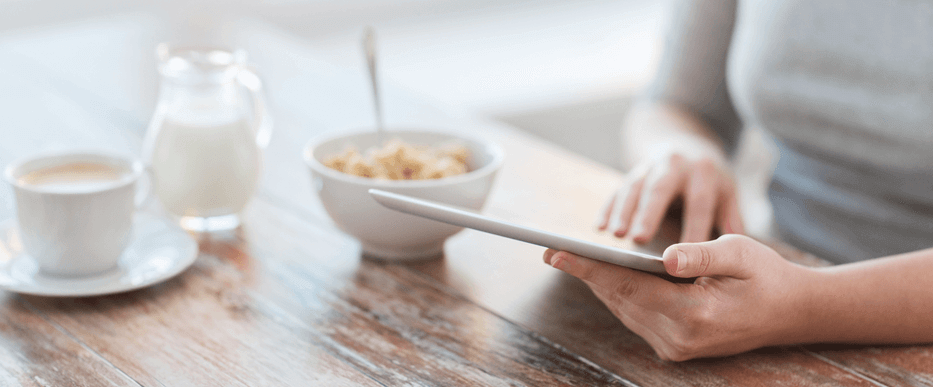 Close-up of a woman using a tablet while sitting at a breakfast table.