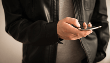 man in a leather jacket texting on a smart phone