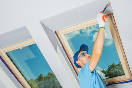 Man painting a high ceiling with two windows.