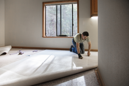 A man laying carpet in a room.