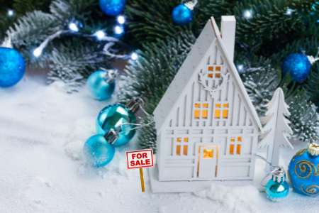 a white wooden home decorated for the holidays with a for sale sign.