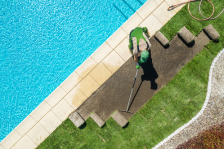 A pool with a man rolling out turf next to it.