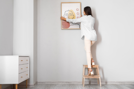 A woman hanging her new wall art in her home.