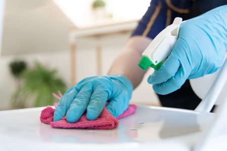 A person with blue gloves using a cleaning spray on a counter.
