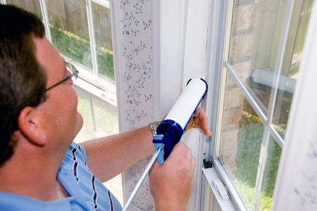 A man caulking his windows to keep heat in- an important home maintenance task.