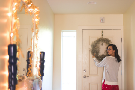 A woman decorating for the holidays by hanging a wreath and lights.
