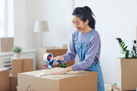 A young woman packing a box because she is moving out of her parents' home.