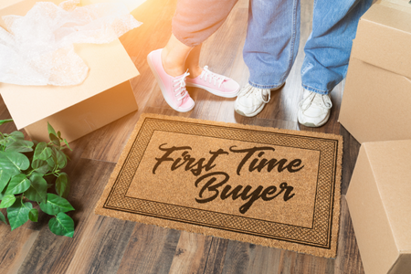 Two people standing next to a door mat that reads "First Time Buyer."