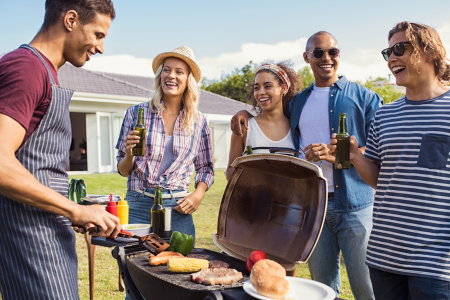A group of young adults watching a man grill during the summer BBQ.