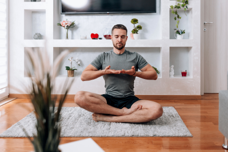 A man deep breathing while doing yoga in his home.