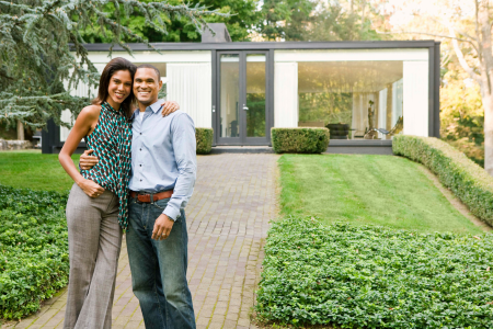 A couple happily standing in front of their home, signifying the benefits of homeownership.