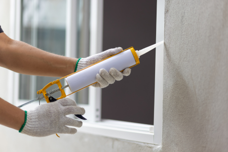 Somebody sealing windows with caulking, an important part of winter home maintenance.