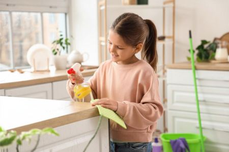 A little girl using a natural cleaner to wipe off the kitchen counter.