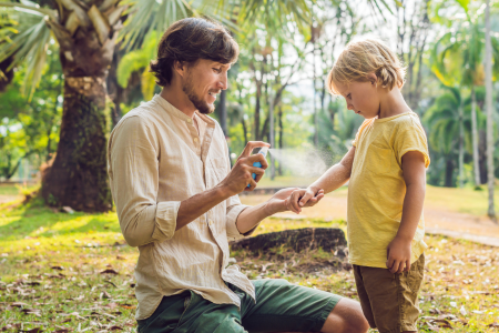 A father spraying natural bug spray on a child.
