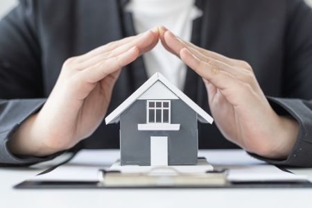 A man with hands over a home for protection, representing landlord insurance.