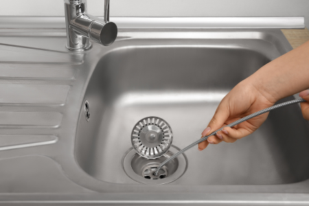 A homeowner snaking a clogged sink drain, a common household problem that you can fix yourself.