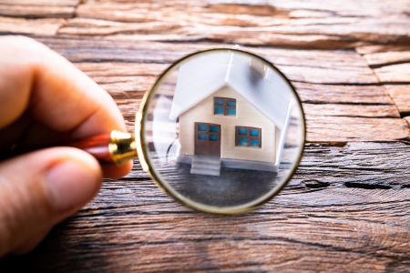 A magnifying glass over a house, symbolic of looking for inspection issues at a property.